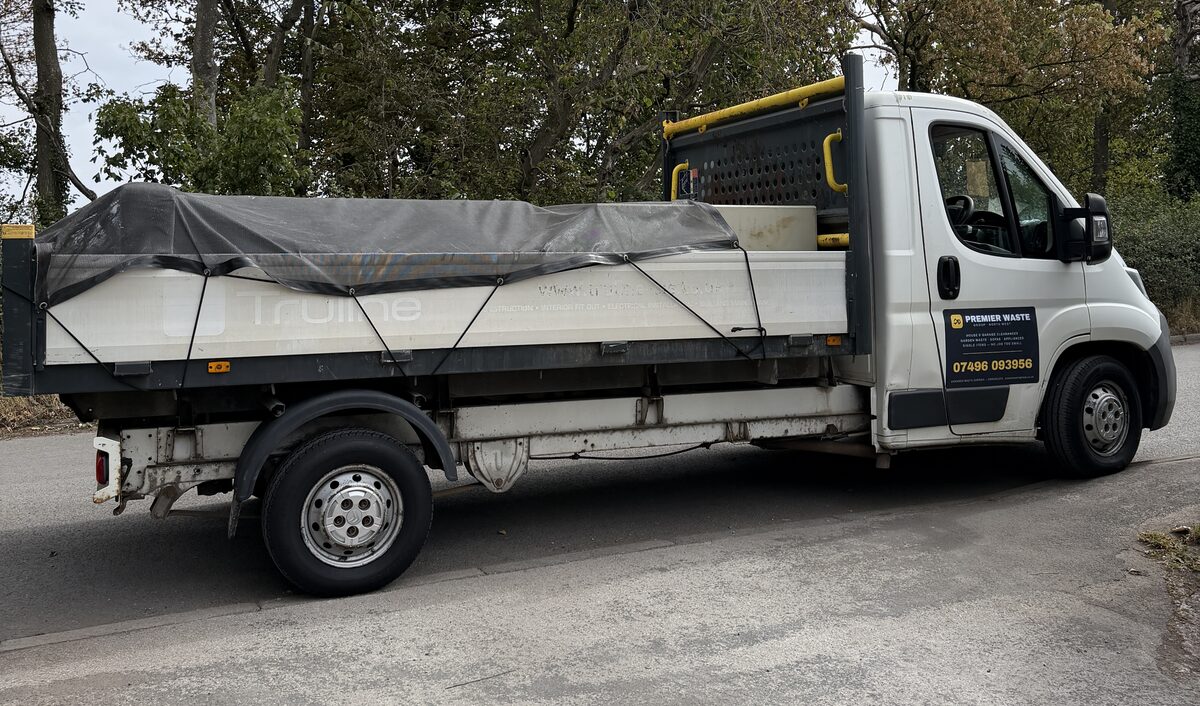 The Premier Waste Group flatbed truck parked at the roadside, fully loaded and sheeted under a netted tarpaulin